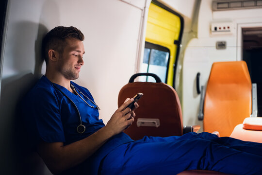 Young doctor in a blue uniform resting and chatting with someone over the phone at night.