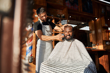 Male barber shaving client beard with electric razor