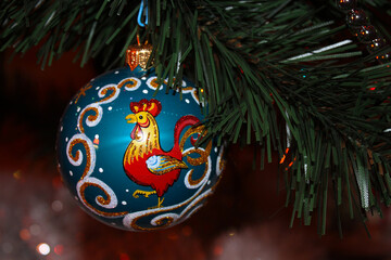 Christmas toy with a picture of a rooster. Christmas ball hanging on a tree branch.