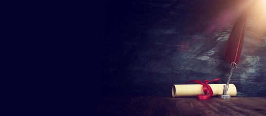 Old feather quill ink pen with inkwell and paper scroll over wooden desk in front of black wall...