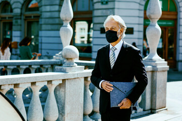 Portrait of a happy senior businessman with face mask walking outside and smiling