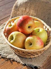 Apples in a wicker basket illuminated by the sun. Plain apples on a rustic table.