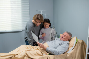 Little girl presents her sick grandfather with a drawing of hers, she came to see him in a hospital.