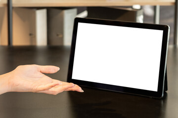 Online meeting. Distance work. Presenting product. Female hand with open palm tablet computer blank screen on wooden table workplace interior copy space.