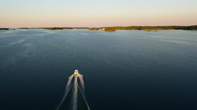 Aerial view following a motorboat, driving in middle of islands, serene, summer sunset, in the Swedish archipelago, Baltic sea, in Sweden - track, drone shot