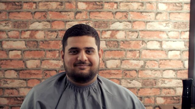 Portrait handsome man with beard showing index finger and winking in barber shop. Satisfied bearded man looking to camera after shaving in barber salon