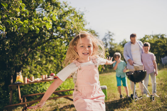 Photo of positive carefree younger kid girl enjoy outdoors summer relax weekend her father brothers cook sausages grill table under green tree