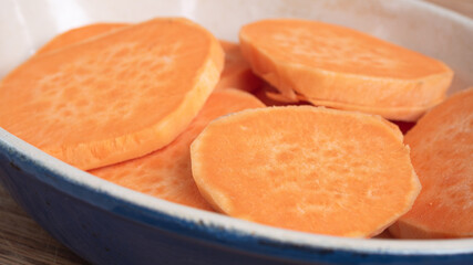 Sliced sweet potato on top of each other in a ceramic casserole. The bright orange herb staple is a healthy replacement for potato or french fries. Concept for displaying food in fall colors.