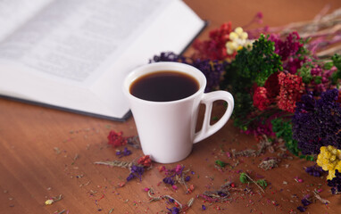 Colorful flowers and a cup of coffee with a book on a wooden background.