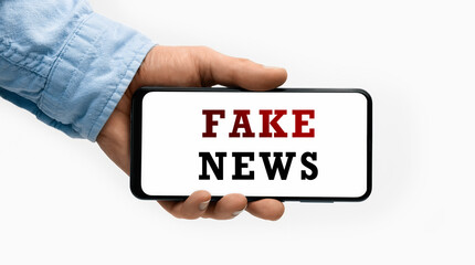 Closeup of a male hand holding Smartphone with text FAKE NEWS on display