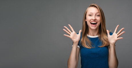 Fototapeta na wymiar Beautiful surprised blonde woman in blue t shirt on gray background. Surprise, excitement concept. Copy space