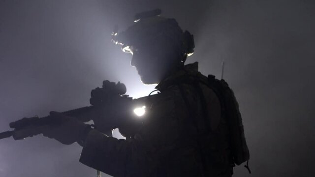 Military soldier with a rifle in his hands and a laser sight on a black background in backlight. The concept of war and hostilities, slow motion