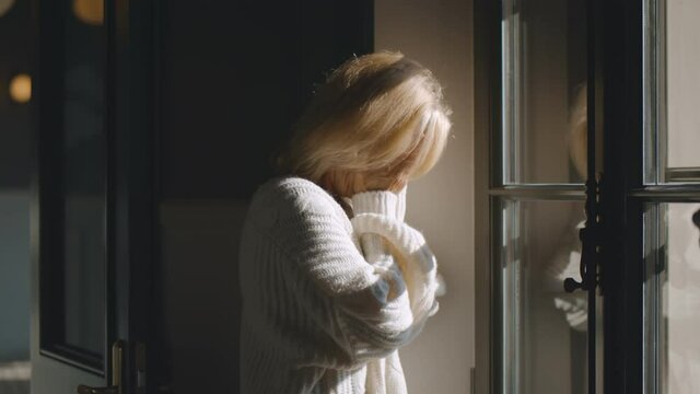 Sad mature caucasian woman looking out of window indoors