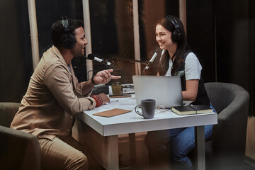 Portait of two happy radio hosts, young man and woman smiling while discussing various topics, moderating a live show in studio