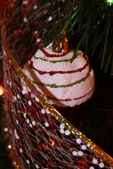 Christmas toy in the form of a cake, hanging on the branch of the tree. Christmas background with a beautiful shiny ribbon and Christmas tree decoration.