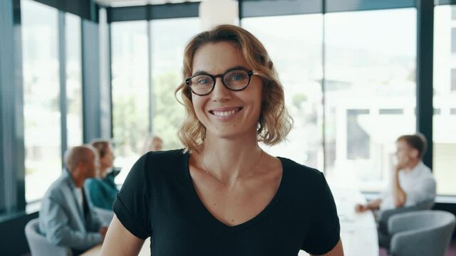 Confident female business professional with eyeglasses. Business woman in casuals with colleagues meeting at the back.
