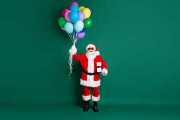 Full length body size view of his he nice handsome cheerful bearded Santa holding in hands bunch helium balls giftbox event festal fast delivery sale isolated over green color background