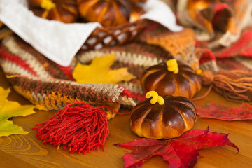 Homemade apple cakes in the shape of pumpkins, cosy colorful shawl or scarf and autumn leaves