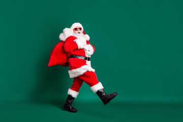 Full length profile photo of retired grandpa white beard walking bearing sack gifts children wear...