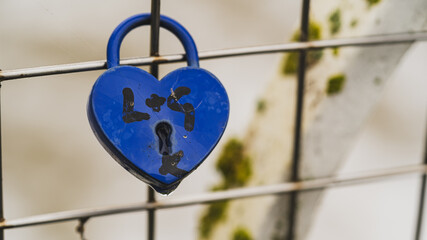 A blue heart-shaped lock on a metal grid of a bridge