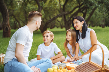 Happy family with two children relaxing on the lawn during a picnic in the green garden