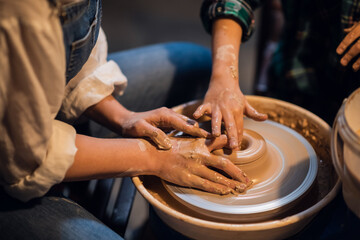 a pretty girl and a blond boy sculpt a plate on a potter's wheel in an art Studio