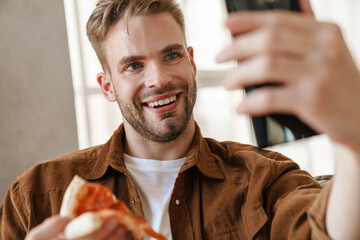 Man eating pizza while talking by videocall by mobile phone