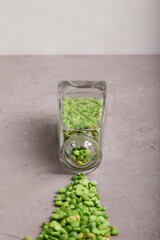 Dried green peas flowing out of crystal cleasr bottle on grey concrete surface. Vertical. Copy space. Selective focus.