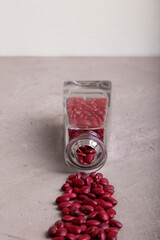Dried red beans flowing out of crystal cleasr bottle on  to grey concrete surface. Vertical. Copy space. Selective focus.