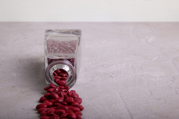 Dried red beans flowing out of crystal cleasr bottle on  to grey concrete surface. Horizontal. Copy space. Selective focus.