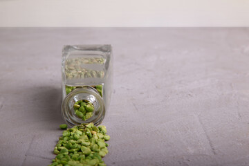  Dried green peas flowing out of crystal cleasr bottle on grey concrete surface. Horizontal. Copy space. Selective focus.