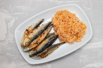 fried small sardines with tomato rice on white dish on ceramic background