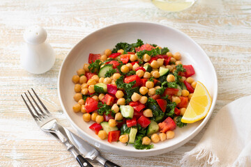 Healthy vegan salad with chickpeas, tomatoes, cucumbers, bell peppers and kale on light wooden background	