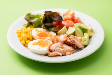 salad salmon with vegetables and boiled egg on white plate on green background