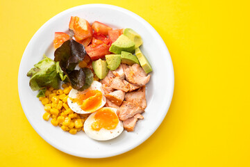 salad salmon with vegetables and boiled egg on white plate on yellow background