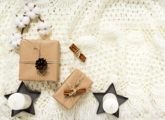 Fototapeta na wymiar Winter composition with gifts, pine cones, cinnamon, a cotton branch on a light knitted blanket. Flat lay, top view, copy space. Warm cozy Christmas