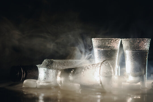 Close-up view of bottle and glasses of vodka standing isolated on black
