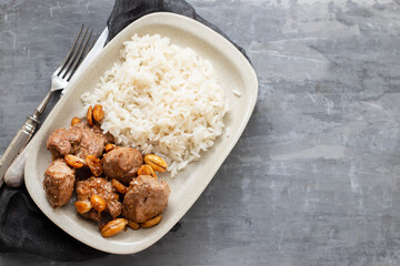 meat with nuts and boiled rice on white plate on ceramic background