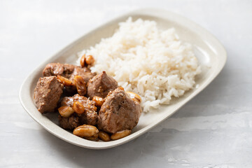 meat with nuts and boiled rice on white plate on ceramic background
