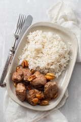 meat with nuts and boiled rice on white plate on ceramic background