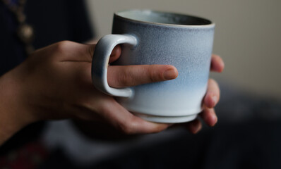 Women holding a mug with tea or coffee, human fingers