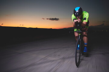 triathlon athlete riding bike fast at night - obrazy, fototapety, plakaty