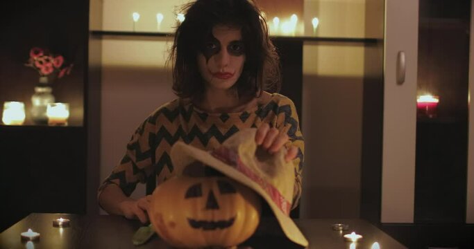 Young female with scary mask and knife sitting on the table with halloween pumpkin in front of her. Halloween day concept. 