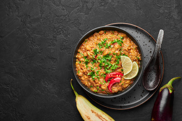 Baingan Bharta or Roasted Mashed Eggplant in black bowl on dark slate table top. Bhurta is indian cuisine puree dish of fire roasted eggplant and masala. Top view. Copy space