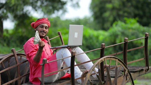 Young Indian farmer sitting on a bull cart and using laptop.