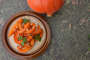 Roasted pumpkin wedges with pine nuts and parsley on a plate. Wooden background
