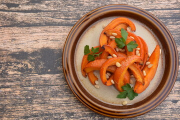 Roasted pumpkin wedges with pine nuts and parsley on a plate. Wooden background. Flat lay