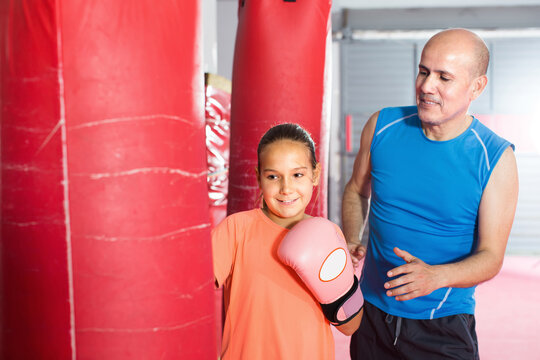 Smiling Teenage Girl Training At Gym On Punching Bag With Instructor