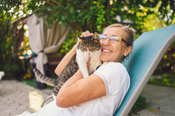 Happy smiling senior elderly woman in glasses relaxing in summer garden outdoors hugging domestic...