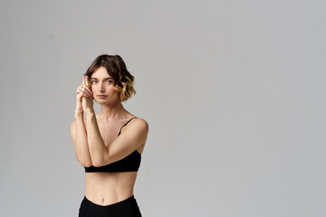 Naklejka premium A slender woman in black leggings on a gray background gestures with her hands gymnastics sports